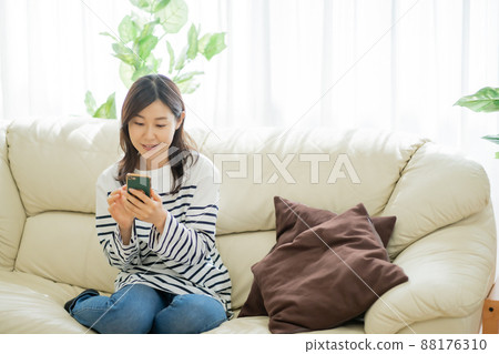 一個三十多歲的女人坐在沙發上看著她的智能手機 88176310