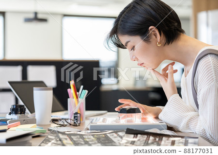 年輕女時裝編輯在辦公桌前用放大鏡看照片底片 88177031