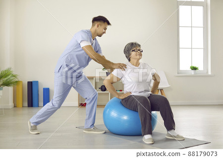 Male doctor with help of fitball trains elderly female patient in rehabilitation clinic. Male doctor with help of fitball trains elderly female patient in rehabilitation clinic. 88179073