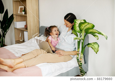 A sweet mom with her little daughter watches a video or movie on a laptop, or works from home. A sweet mom with her little daughter watches a video or movie on a laptop, or works from home. 88179660