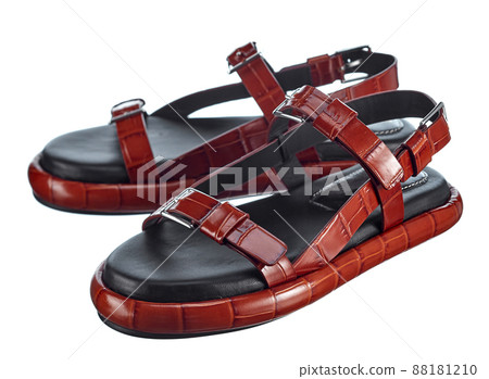 Pair of high-quality summer sandals made of red-brown crocodile leather straps, on a soft leather sole, isolated on a white background. Comfortable shoes for summer walks. Pair of high-quality summer sandals made of red-brown crocodile leather straps, on a soft leather sole, isolated on a white background. Comfortable shoes for summer walks. 88181210