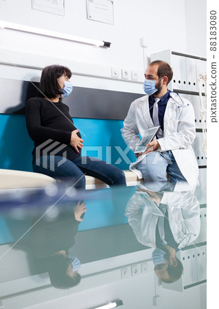 Doctor showing human skeleton on tablet to pregnant adult at appointment during pandemic. Patient with pregnancy belly and physician talking about osteopathy scan in medical cabinet. Doctor showing human skeleton on tablet to pregnant adult at appointment during pandemic. Patient with pregnancy belly and physician talking about osteopathy scan in medical cabinet. 88183080