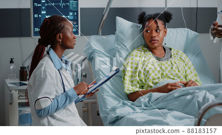 General practitioner discussing with ill patient about treatment and medicine while looking at heart rate monitor to measure pulse and heartbeat. Young woman receiving medical care General practitioner discussing with ill patient about treatment and medicine while looking at heart rate monitor to measure pulse and heartbeat. Young woman receiving medical care 88183157
