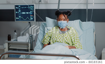 Portrait of african american patient wearing face mask, laying in hospital ward bed. Young woman with disease trying to heal during coronavirus pandemic. Sick person with protection 88183161