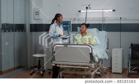 African american doctor doing consultation with patient in bed while medical assistant helping with oximeter to measure oxygen saturation. Medic consulting person with IV drip bag. 88183163