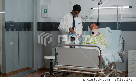 Specialist explaining radiography to woman with neck collar in hospital ward bed. Medical physician showing x ray diagnosis to injured patient wearing cervical foam. Healthcare exam Specialist explaining radiography to woman with neck collar in hospital ward bed. Medical physician showing x ray diagnosis to injured patient wearing cervical foam. Healthcare exam 88183173