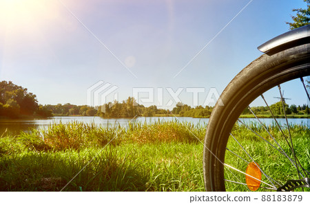 Part of the front wheel of a bicycle on a meadow in front of a lake in summer in Germany Part of the front wheel of a bicycle on a meadow in front of a lake in summer in Germany 88183879