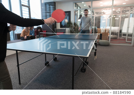 Two young start up business man playing table tennis at modern creative office space people group have meeting and brainstorming in background Two young start up business man playing table tennis at modern creative office space people group have meeting and brainstorming in background 88184590