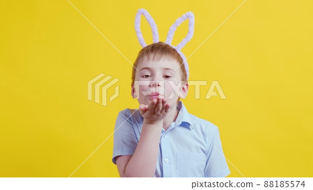 Close-up of a happy boy with rabbit ears on a yellow background. The boy blows a kiss. Easter Close-up of a happy boy with rabbit ears on a yellow background. The boy blows a kiss. Easter 88185574