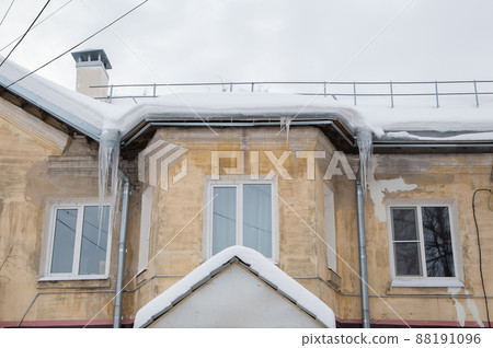 Multiple ice icicles hang from a drainpipe at the edge of the roof. Multiple ice icicles hang from a drainpipe at the edge of the roof. 88191096