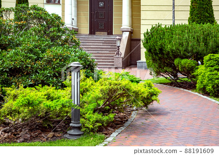 curved pedestrian pavement of stone brick tiles in backyard with landscape and green bushes deciduous and evergreen pine bushes, landscape with ground lanter on background is mansion, nobody. curved pedestrian pavement of stone brick tiles in backyard with landscape and green bushes deciduous and evergreen pine bushes, landscape with ground lanter on background is mansion, nobody. 88191609