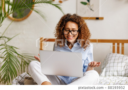 Joyful emotional african american teenage girl feeling excited while sitting on bed with laptop during video call 88193932