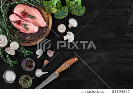 Raw chicken breast fillets on wooden cutting board with herbs, spices and vegetables. Top view with copy space Raw chicken breast fillets on wooden cutting board with herbs, spices and vegetables. Top view with copy space 88194225