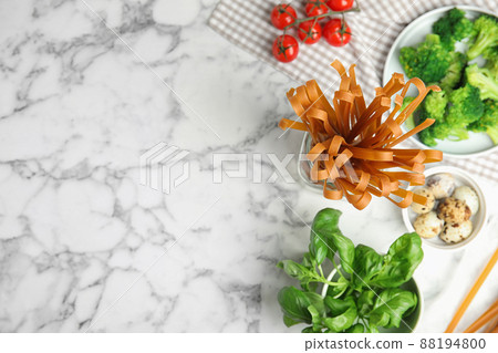 Uncooked buckwheat noodles and fresh ingredients on white marble table, flat lay. Space for text 88194800