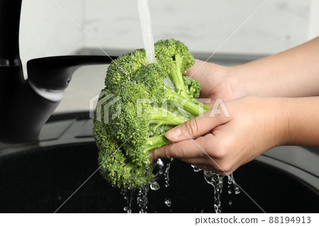 Woman washing fresh green broccoli in kitchen sink, closeup 88194913
