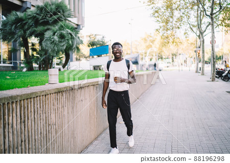 Cheerful African American tourist walking on street with coffee 88196298