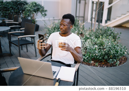 Concentrated dark skinned freelancer hipster guy checking notifications on cellular 88196310