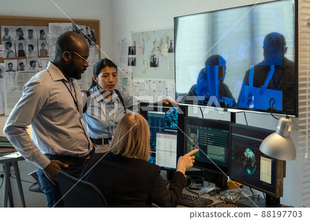 Mature FBI agent showing two young subordinates photo of criminal on screen 88197703