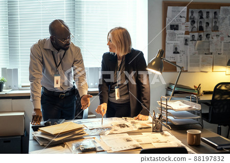 Two interracial agents of FBI discussing criminal profiles at meeting in bureau 88197832