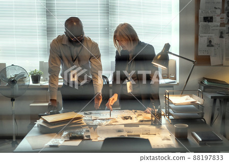 Two confident FBI agents bending over desk with criminal profiles and evidences 88197833