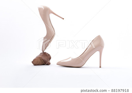 Elegant beige high heels. Beige patent leather shoes. One shoe floats in the air, resting on a stone. The concept of lightness, weightlessness. antigravity 88197918