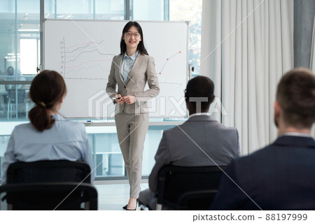 Happy young Asian female speaker presenting financial information to colleagues 88197999