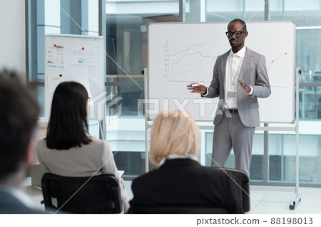 Confident teacher in grey suit explaining audience graphic data on whiteboard 88198013