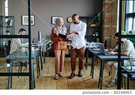 Young confident economist pointing at financial document held by colleague 88198063