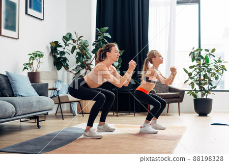 Mother and daughter doing squats. Home training. Mother and daughter doing squats. Home training. 88198328