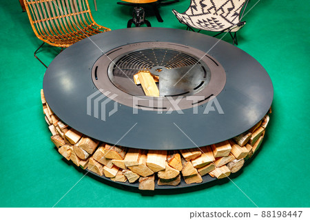 Multifunctional round garden brazier with a dining area with a grill and a firewood shed around the perimeter. Multifunctional round garden brazier with a dining area with a grill and a firewood shed around the perimeter. 88198447