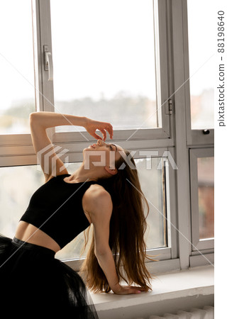 Ballerina wearing black dress sitting on windows and touching hair 88198640