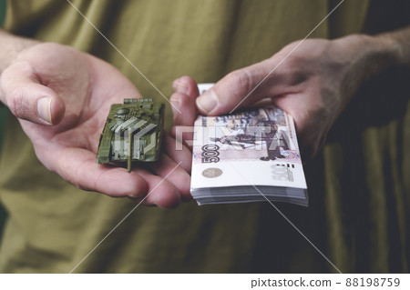 Russian rubles banknotes and toy tank in hands during the war in Ukraine. Inflation, sanctions and the fall of the Russian economy concept. Falling cash savings and budget 88198759
