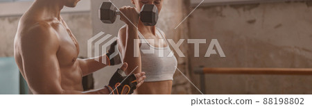 Muscular man in the gym with athletic woman performing sports exercises 88198802