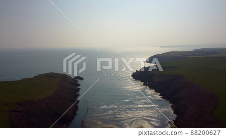 Atlantic Ocean cliffs with sun glare in drone flight over Stradbally Cove, Cooper Coast, Waterford, Ireland. Atlantic Ocean cliffs with sun glare in drone flight over Stradbally Cove, Cooper Coast, Waterford, Ireland. 88200627