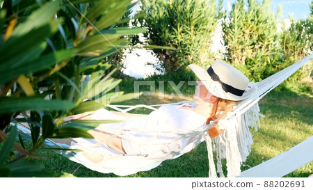 female age 50-60 in a straw hat is resting in a hammock around the palm trees and enjoying the female age 50-60 in a straw hat is resting in a hammock around the palm trees and enjoying the 88202691