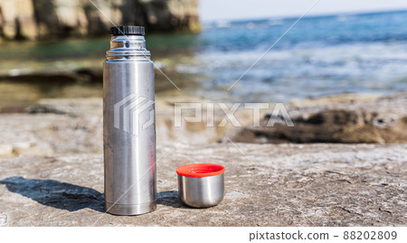 Thermos and mug on stone on the beach at sunset near the sea 88202809