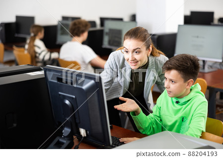 Smiling female teacher talking to happy preteen student in computer class 88204193