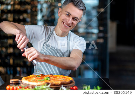A man in apron making vegetarian pizza with cherry tomatos 88205149