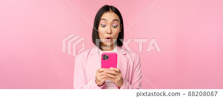 Portrait of asian businesswoman with surprised face, using smartphone app, wearing business suit. Korean girl with mobile phone and excited face expression, pink background Portrait of asian businesswoman with surprised face, using smartphone app, wearing business suit. Korean girl with mobile phone and excited face expression, pink background 88208087