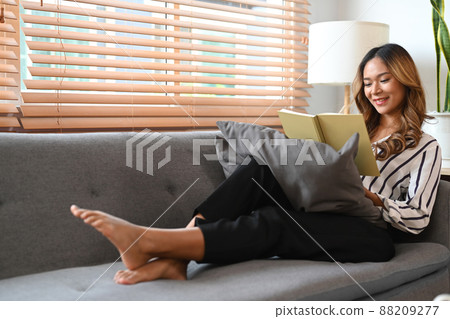 Pretty woman reading a book on sofa while spending leisure time at home. 88209277