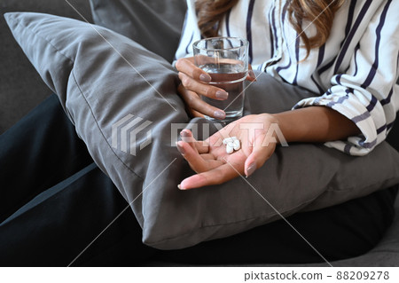 Cropped image of woman holding  pills and a glass of water in hand. Healthcare, medicine, treatment, therapy concept. 88209278