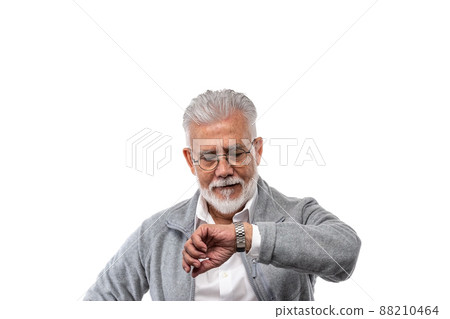 An elderly stylish man gray-haired and with a beard on a white isolated background looks at his watch. The concept of punctuality and discipline. 88210464