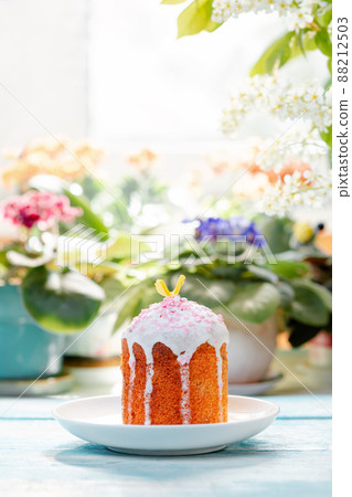 One decorated Easter bread on a plate. In the background-plants and flowers. Vertical orientation. Easter holiday. Copy space One decorated Easter bread on a plate. In the background-plants and flowers. Vertical orientation. Easter holiday. Copy space 88212503