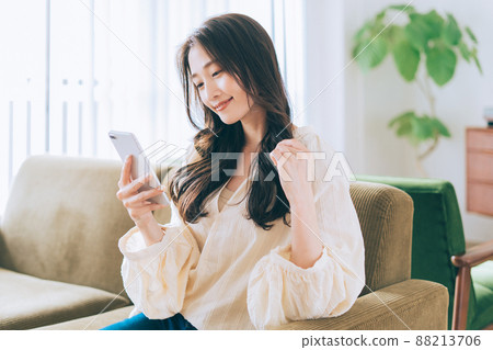 Woman sitting on a sofa and looking at a smartphone 88213706
