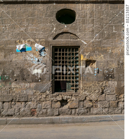 Old abandoned stone bricks wall with one closed grunge broken wooden window covered by wooden grid 88213887