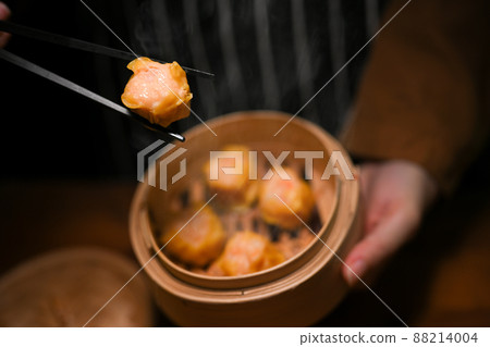 Women eating steamed shrimp dumplings with chopsticks 88214004