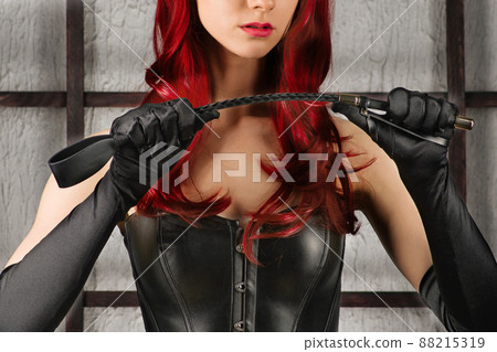 Red-haired woman in a leather corset holds spank. Red-haired woman in a leather corset holds spank. 88215319