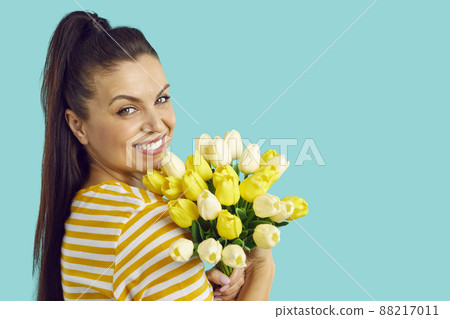 Portrait of a cheerful young woman with a bouquet of yellow tulips isolated on blue background. Cute girl smiling on blank wall background, copy space. 88217011