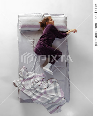 Creative portrait of young girl wearing wine color homewear, pajamas sleeping in big bed. Concept of health, home interior, relax time, family, dreams Creative portrait of young girl wearing wine color homewear, pajamas sleeping in big bed. Concept of health, home interior, relax time, family, dreams 88217546