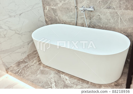 Luxury big oval bathtub in bathroom with black and white marble tiles on walls and floor. Luxury big oval bathtub in bathroom with black and white marble tiles on walls and floor. 88218936